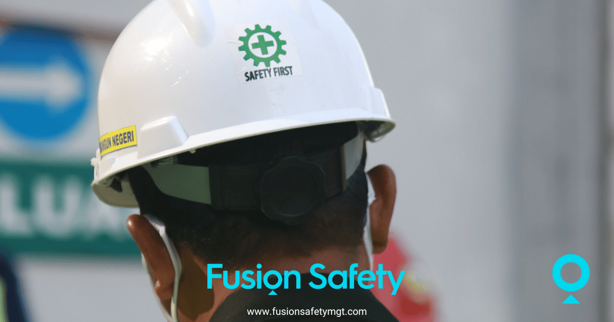 Back of man's head in Indonesia wearing white safety helmet with safety first written on it in green and yellow high visibility vest.